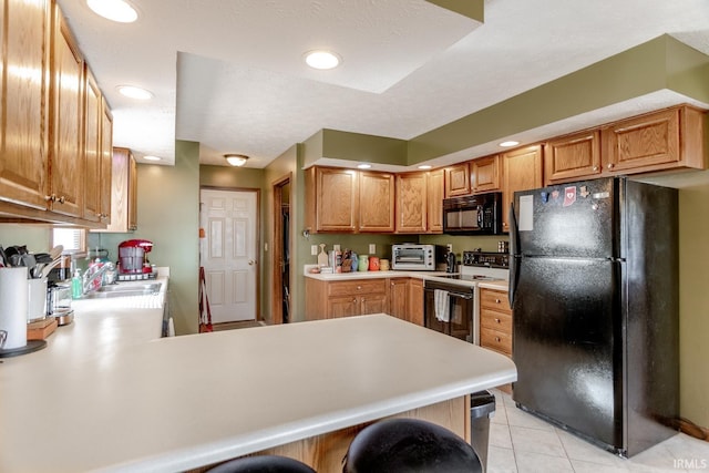 kitchen featuring a toaster, light countertops, light tile patterned floors, a peninsula, and black appliances