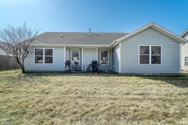 rear view of property featuring a yard, fence, and a shingled roof