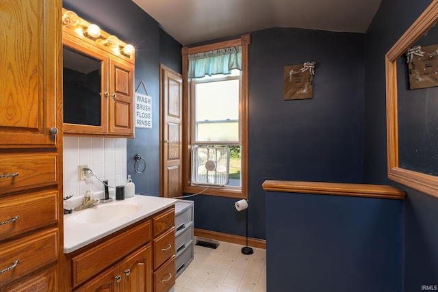 bathroom with baseboards, backsplash, vanity, and vaulted ceiling