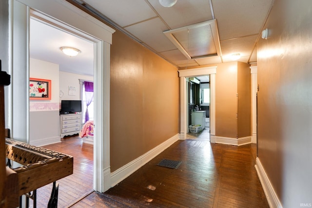 hall with hardwood / wood-style floors, attic access, baseboards, and visible vents