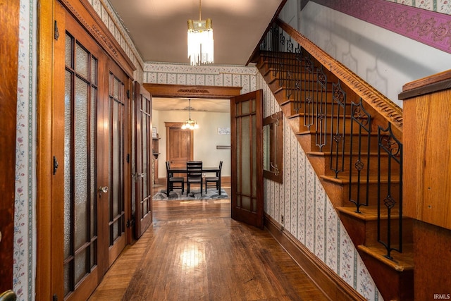 interior space featuring baseboards, wallpapered walls, stairs, wood-type flooring, and a notable chandelier