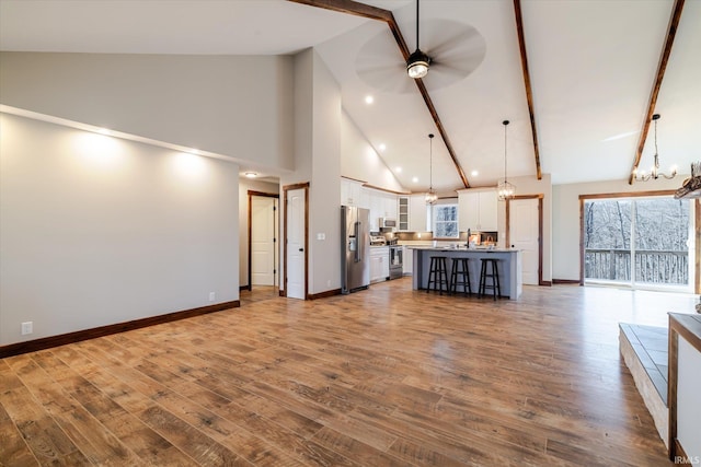 unfurnished living room featuring beamed ceiling, baseboards, wood finished floors, and ceiling fan with notable chandelier