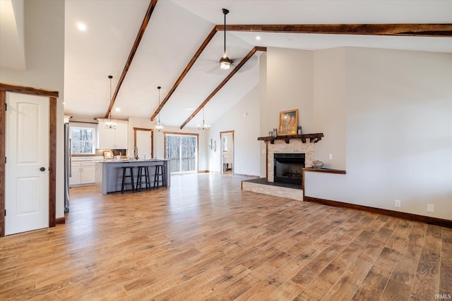 unfurnished living room with a stone fireplace, beamed ceiling, light wood-style floors, and baseboards