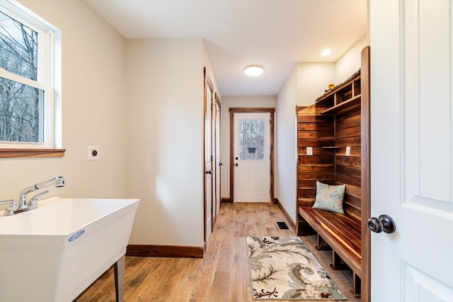 mudroom featuring a sink, baseboards, a healthy amount of sunlight, and light wood-style flooring