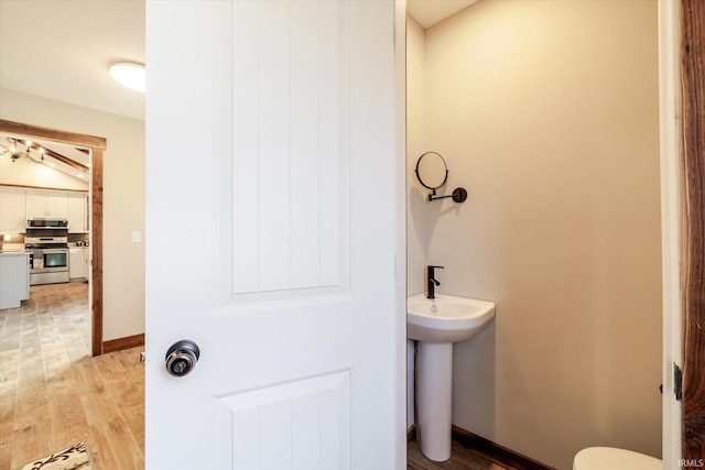 half bath featuring a sink, baseboards, and wood finished floors