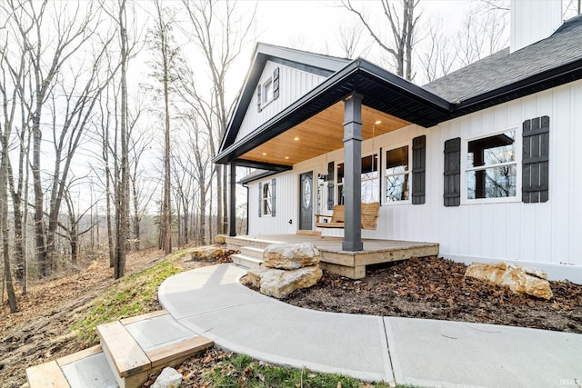 doorway to property featuring a porch and roof with shingles