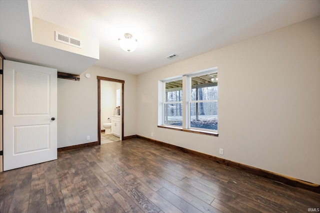 unfurnished bedroom with hardwood / wood-style floors, baseboards, visible vents, and ensuite bathroom