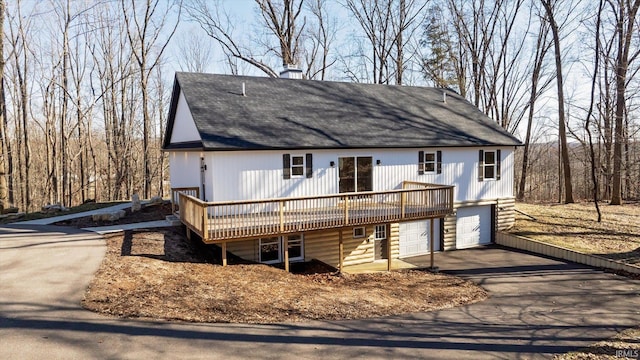 view of front of house featuring an attached garage, a shingled roof, a chimney, a deck, and aphalt driveway