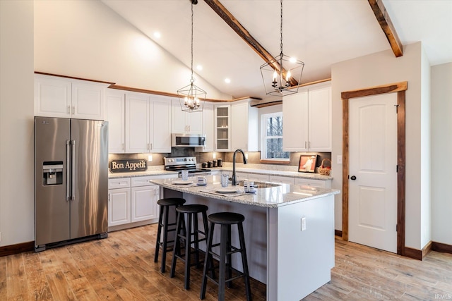 kitchen with light wood finished floors, a center island with sink, white cabinets, stainless steel appliances, and a sink