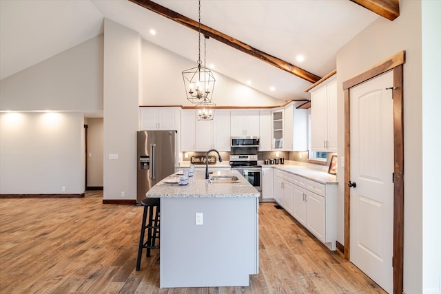 kitchen featuring a kitchen bar, beam ceiling, a sink, appliances with stainless steel finishes, and white cabinets