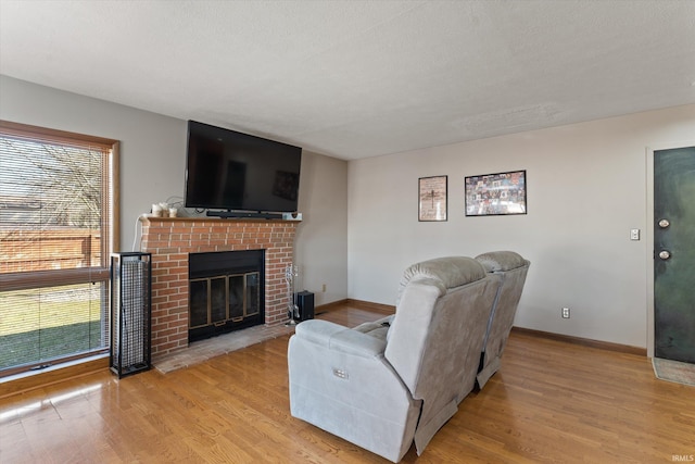 living room with a brick fireplace, baseboards, and light wood-style floors