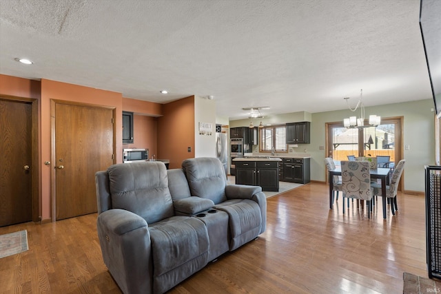 living room with baseboards, recessed lighting, light wood-style flooring, a notable chandelier, and a textured ceiling