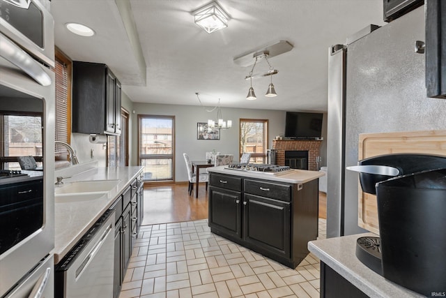 kitchen featuring an inviting chandelier, a sink, stainless steel appliances, brick patterned floor, and dark cabinets