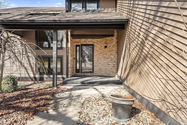 entrance to property featuring brick siding and a shingled roof