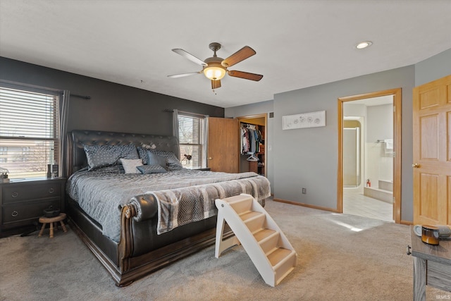 bedroom featuring a walk in closet, ensuite bath, a closet, baseboards, and light colored carpet