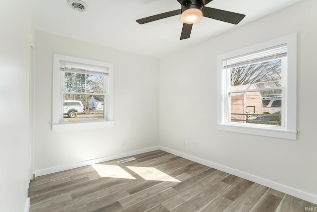 empty room featuring visible vents, plenty of natural light, baseboards, and wood finished floors