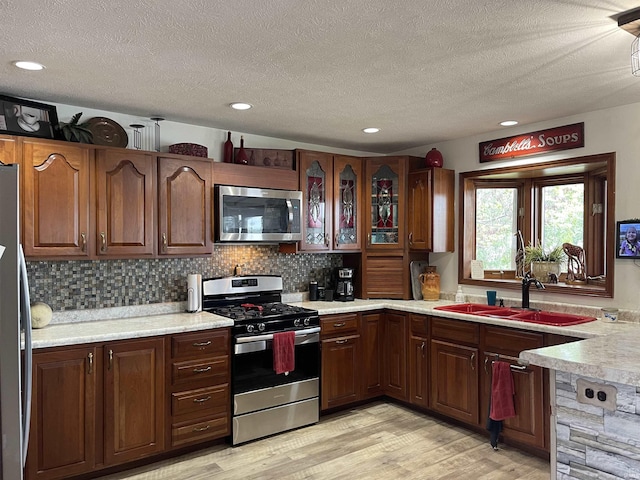 kitchen with light wood-type flooring, a sink, backsplash, appliances with stainless steel finishes, and light countertops