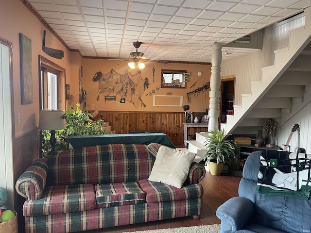 living area featuring a wainscoted wall, wood walls, stairs, and ceiling fan