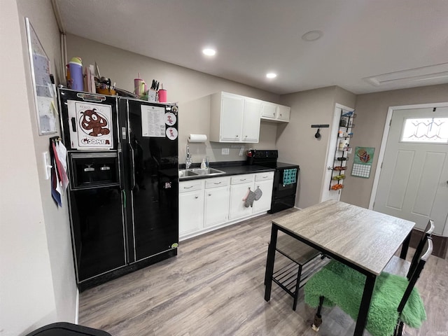 kitchen featuring dark countertops, light wood finished floors, white cabinets, black appliances, and a sink