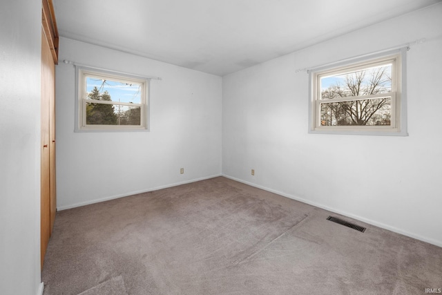 empty room with a wealth of natural light, visible vents, and carpet flooring