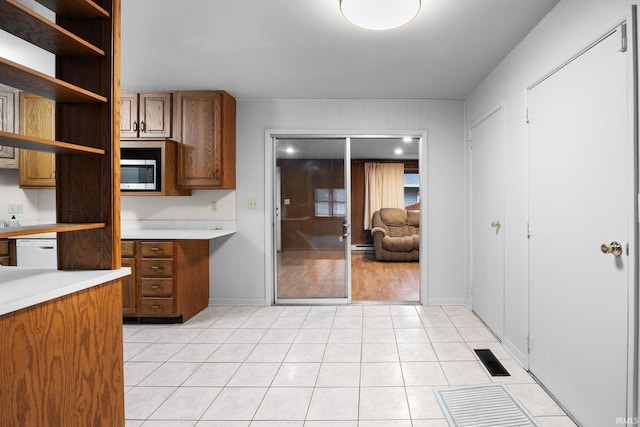 kitchen with brown cabinetry, stainless steel microwave, white dishwasher, and light countertops