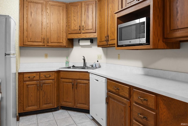 kitchen featuring light countertops, light tile patterned floors, brown cabinetry, white appliances, and a sink