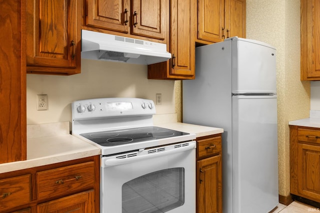 kitchen with white appliances, brown cabinetry, light countertops, and under cabinet range hood