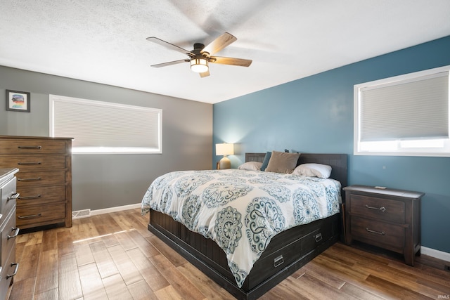 bedroom featuring ceiling fan, baseboards, a textured ceiling, and wood finished floors