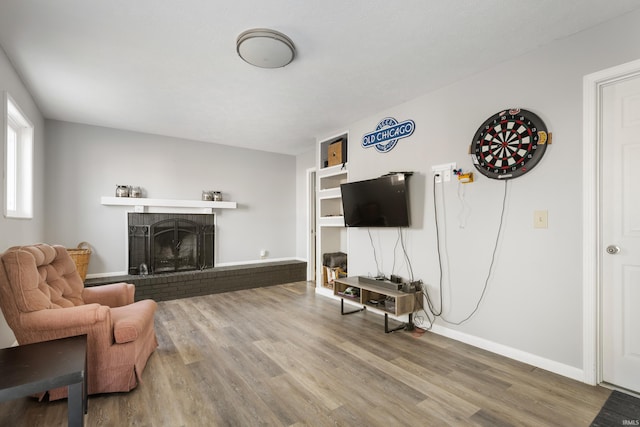 living area featuring a brick fireplace, baseboards, and wood finished floors