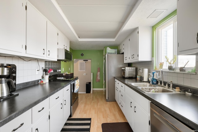 kitchen featuring light wood-type flooring, a sink, dark countertops, white cabinetry, and appliances with stainless steel finishes