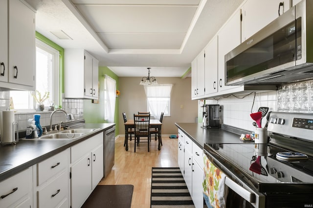 kitchen featuring light wood-type flooring, a sink, stainless steel appliances, white cabinets, and a raised ceiling