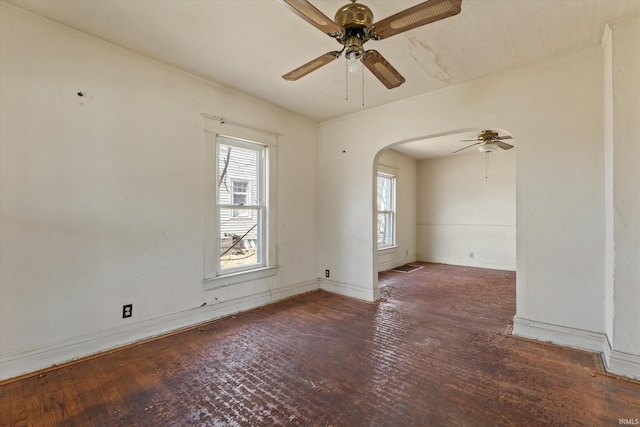 spare room featuring baseboards, arched walkways, wood-type flooring, and ceiling fan