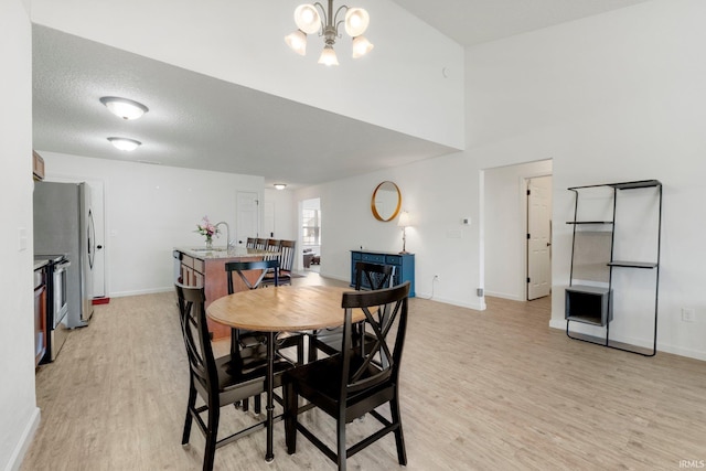 dining space featuring baseboards, light wood-style floors, an inviting chandelier, and a textured ceiling