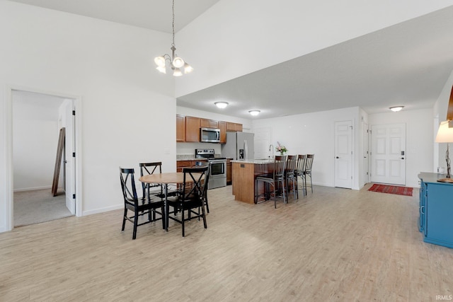 dining area featuring baseboards, a notable chandelier, a high ceiling, and light wood-style flooring