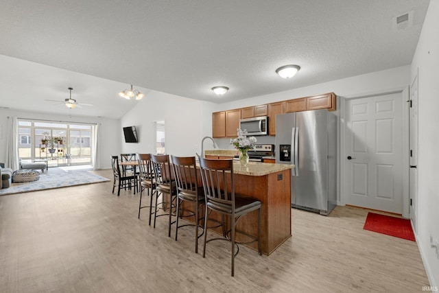 kitchen with visible vents, open floor plan, a breakfast bar area, brown cabinets, and stainless steel appliances