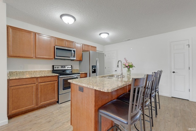 kitchen with light wood-style flooring, a kitchen island with sink, appliances with stainless steel finishes, and a sink