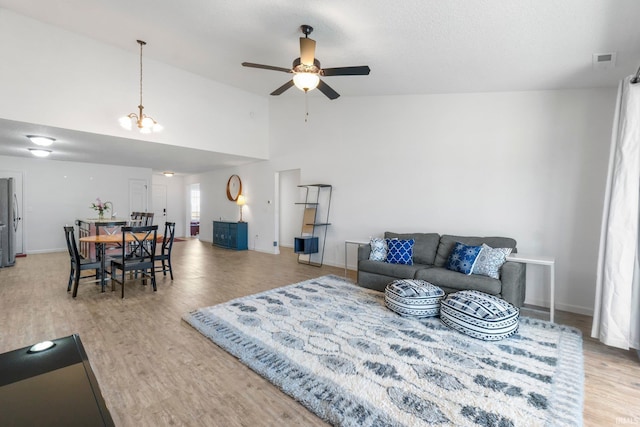 living room featuring visible vents, baseboards, light wood-type flooring, ceiling fan with notable chandelier, and high vaulted ceiling