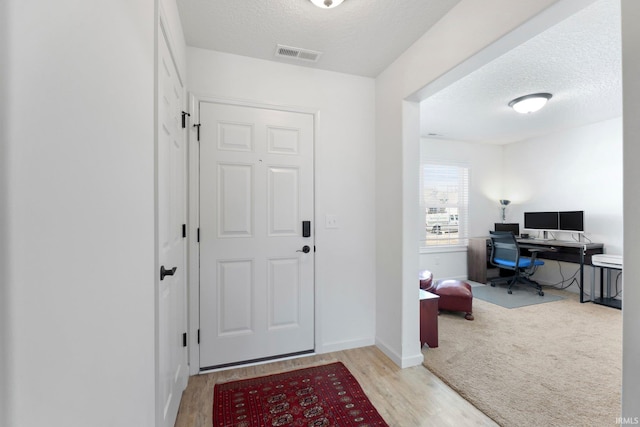 foyer with visible vents, a textured ceiling, baseboards, and wood finished floors