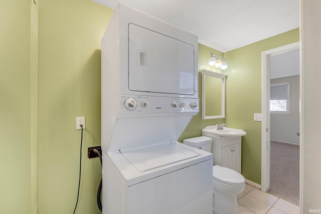 laundry area featuring light tile patterned floors, baseboards, laundry area, a sink, and stacked washer and clothes dryer