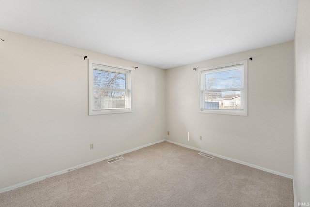 carpeted spare room featuring a healthy amount of sunlight, visible vents, and baseboards