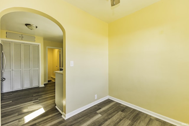 spare room featuring baseboards, arched walkways, and dark wood-type flooring