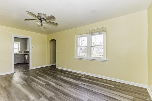 unfurnished room with arched walkways, dark wood finished floors, baseboards, and a ceiling fan