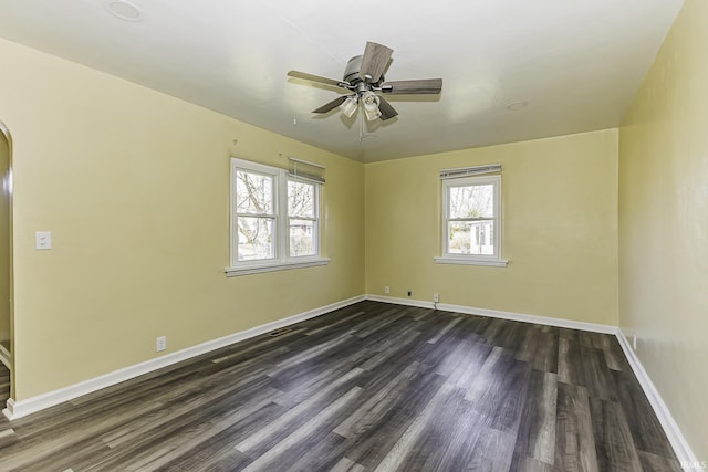 empty room with visible vents, baseboards, dark wood finished floors, arched walkways, and ceiling fan