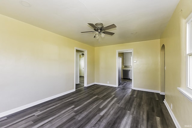 spare room with dark wood finished floors, arched walkways, baseboards, and ceiling fan