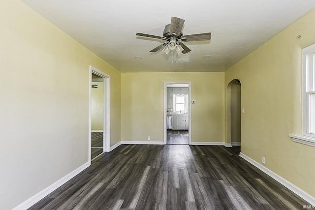 spare room featuring a ceiling fan, dark wood finished floors, baseboards, and arched walkways