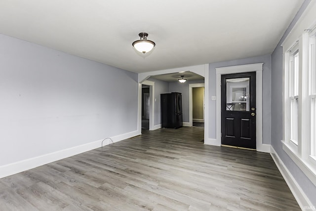 empty room featuring baseboards, arched walkways, and wood finished floors