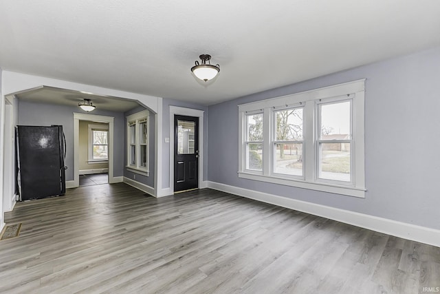 unfurnished living room with wood finished floors, a healthy amount of sunlight, and baseboards