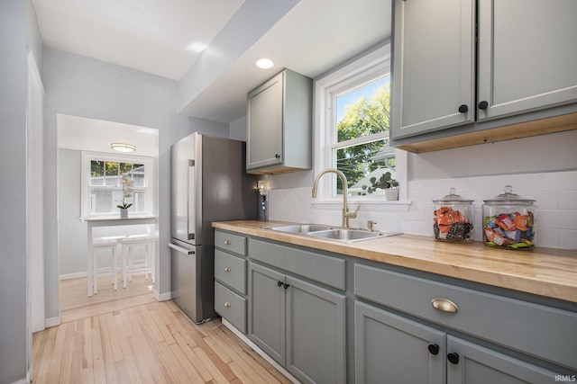 kitchen featuring gray cabinets, a sink, backsplash, light wood-style floors, and butcher block counters