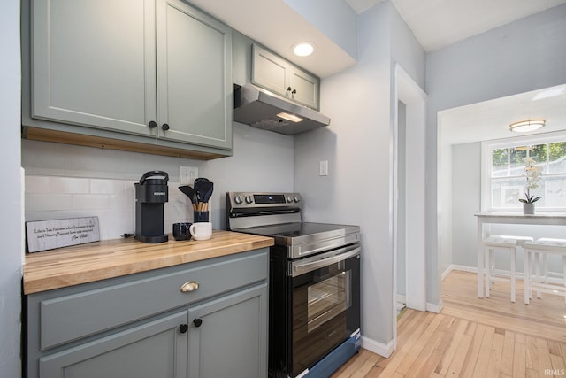 kitchen featuring stainless steel electric range, gray cabinetry, decorative backsplash, under cabinet range hood, and butcher block counters