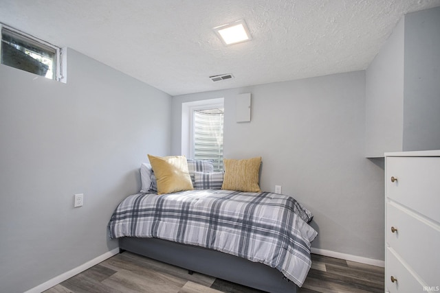 bedroom featuring visible vents, a textured ceiling, baseboards, and wood finished floors